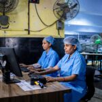 Two female textile workers using computers in a factory setting.