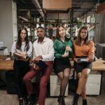 A diverse group of young professionals posing in a modern office setting, holding folders and looking confident.